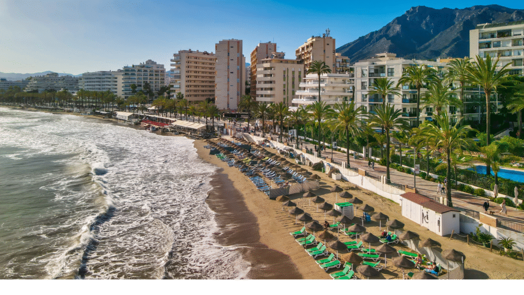 Beachfront in Marbella, Costa del Sol, Spain — golden sand, palm trees, and Mediterranean waves along the city promenade—Quintessentia Property Advisors