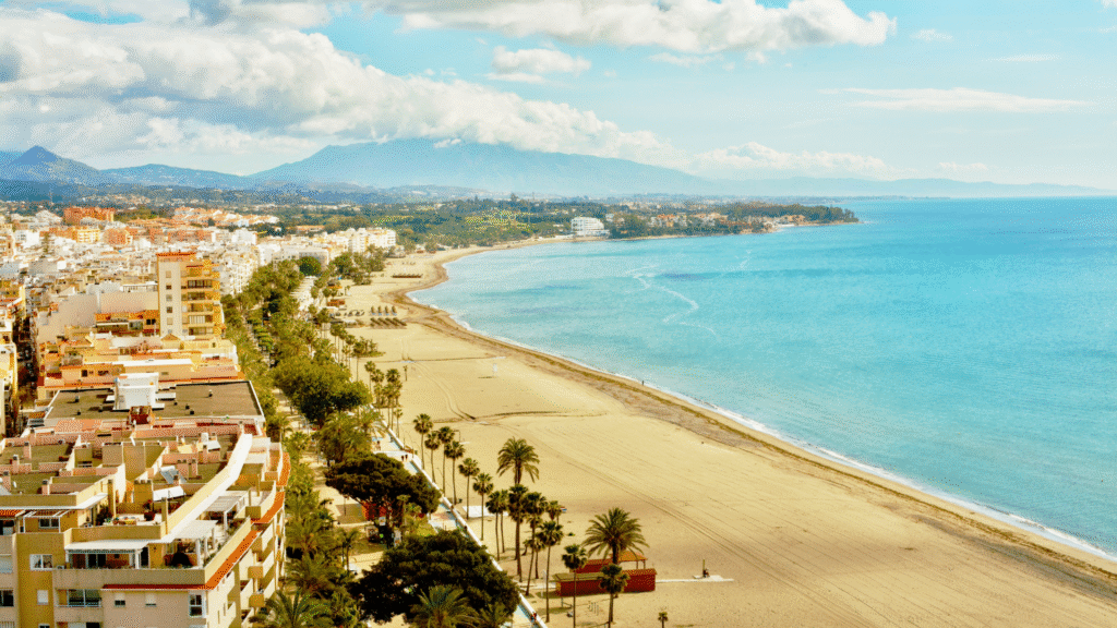 Aerial view of Estepona beachfront, Costa del Sol — golden sand, Mediterranean Sea, and palm-lined promenade near luxury apartments and villas-Quintessentia Propety Advisors