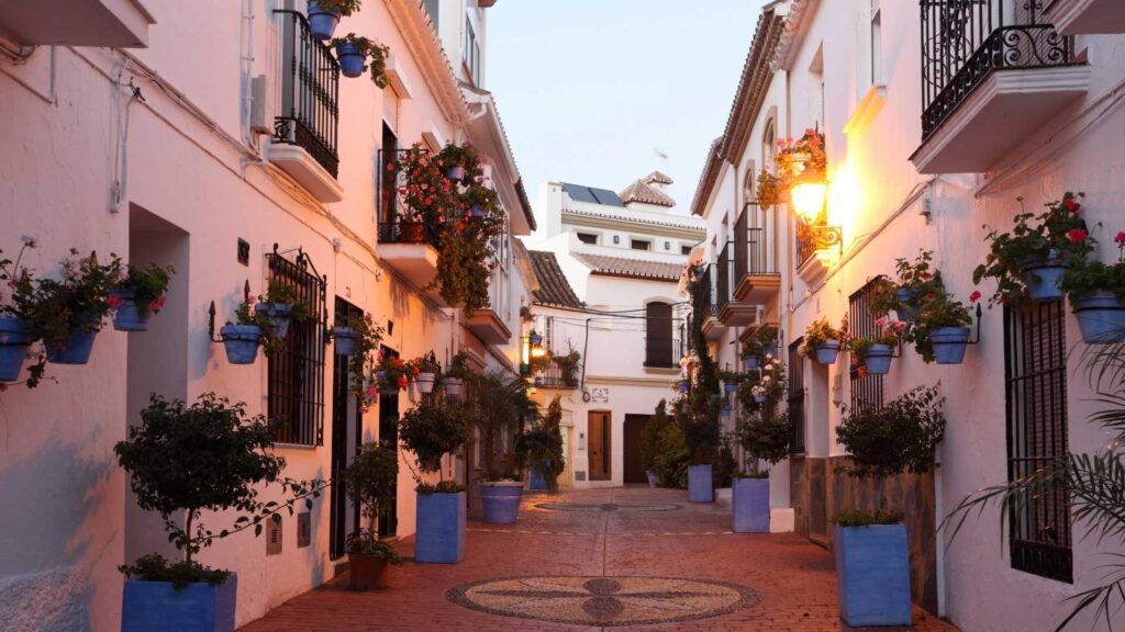 Charming traditional street in Estepona Old Town with whitewashed houses and flower pots, highlighting the area’s appeal for property investors in southern Spain and illustrating the average rental yields for properties in Estepona.