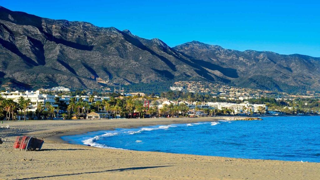 Beautiful beach and coastal skyline in Nueva Andalucía with mountains in the background, showcasing area for new property developments in Marbella