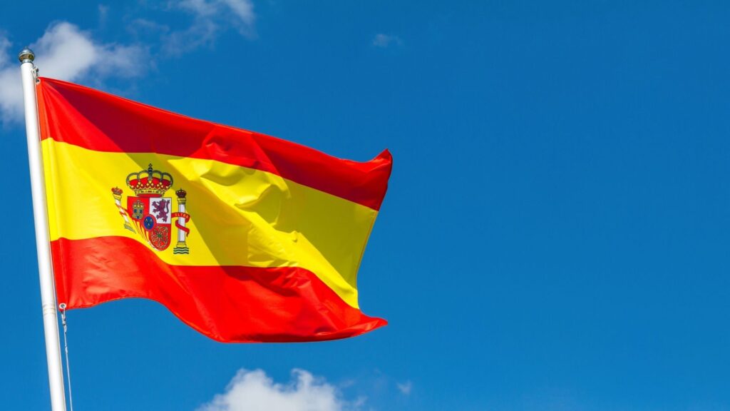 Spanish flag waving against blue sky, symbolizing property investment and real estate opportunities in Spain.