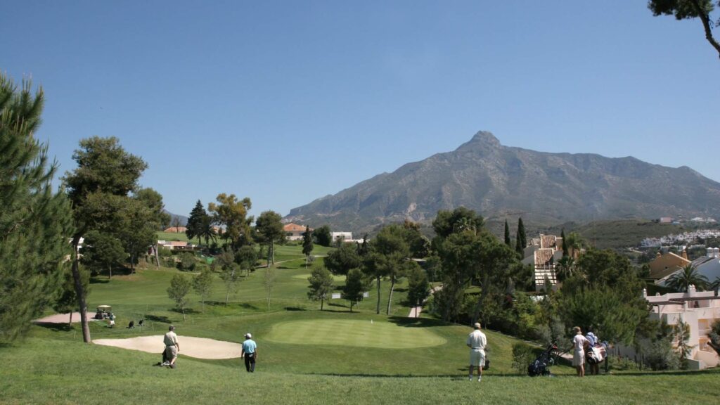 Golfers playing on a lush golf course in Marbella with panoramic views of La Concha mountain under a clear blue sky on the Costa del Sol.
