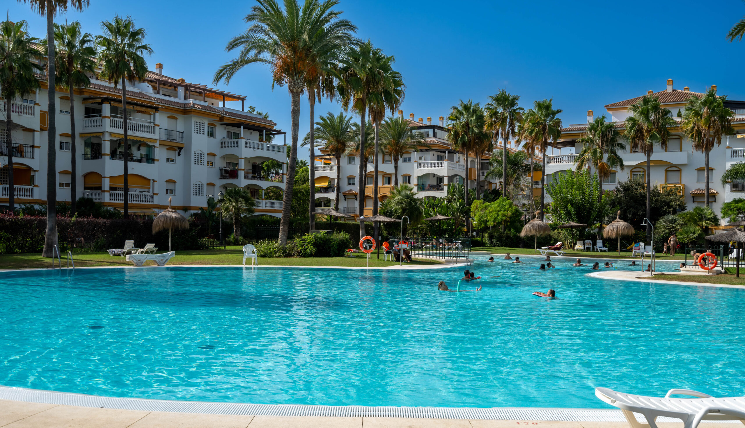 Large communal swimming pool surrounded by palm trees and Mediterranean apartments in Marbella