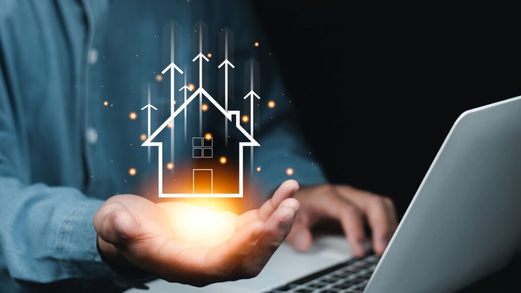 “Person holding a glowing digital house icon with upward arrows, symbolising rising property value and real estate investment growth.”