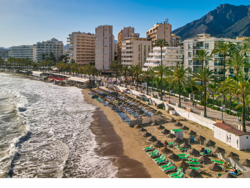 Beachfront in Marbella, Costa del Sol, Spain — golden sand, palm trees, and Mediterranean waves along the city promenade—Quintessentia Property Advisors