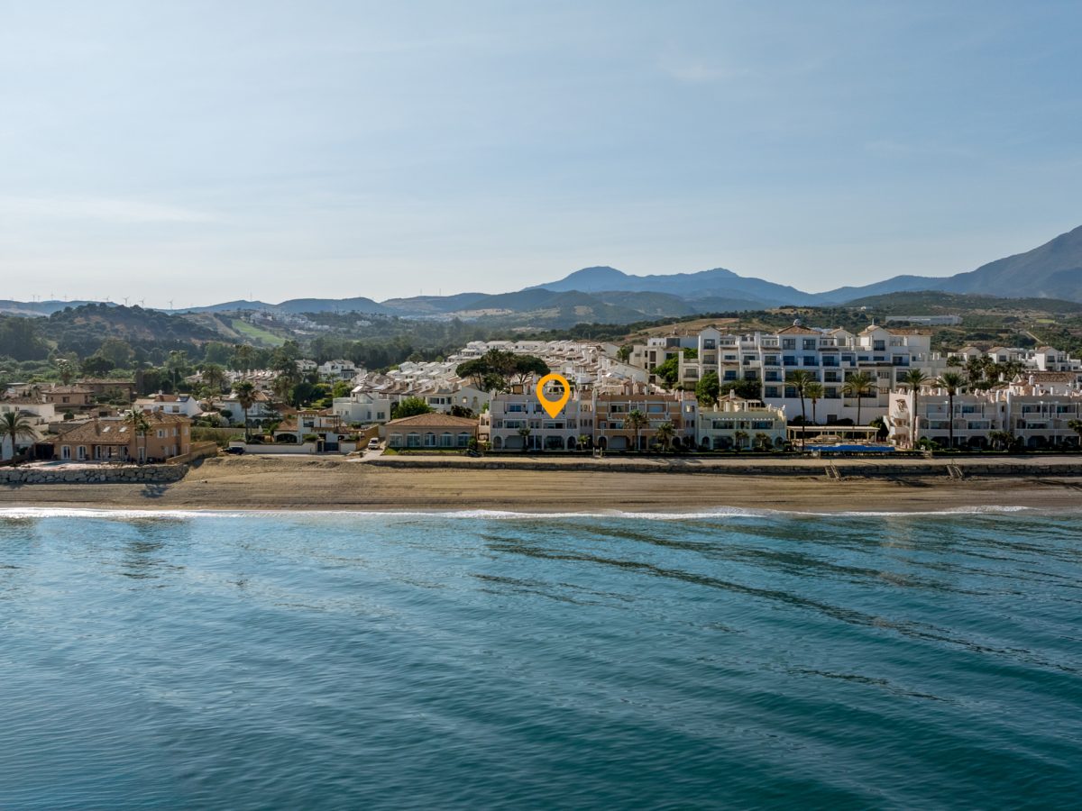 Drone view of Playa del Moral beachfront apartment complex with sea and mountain backdrop in Costa del Sol.
