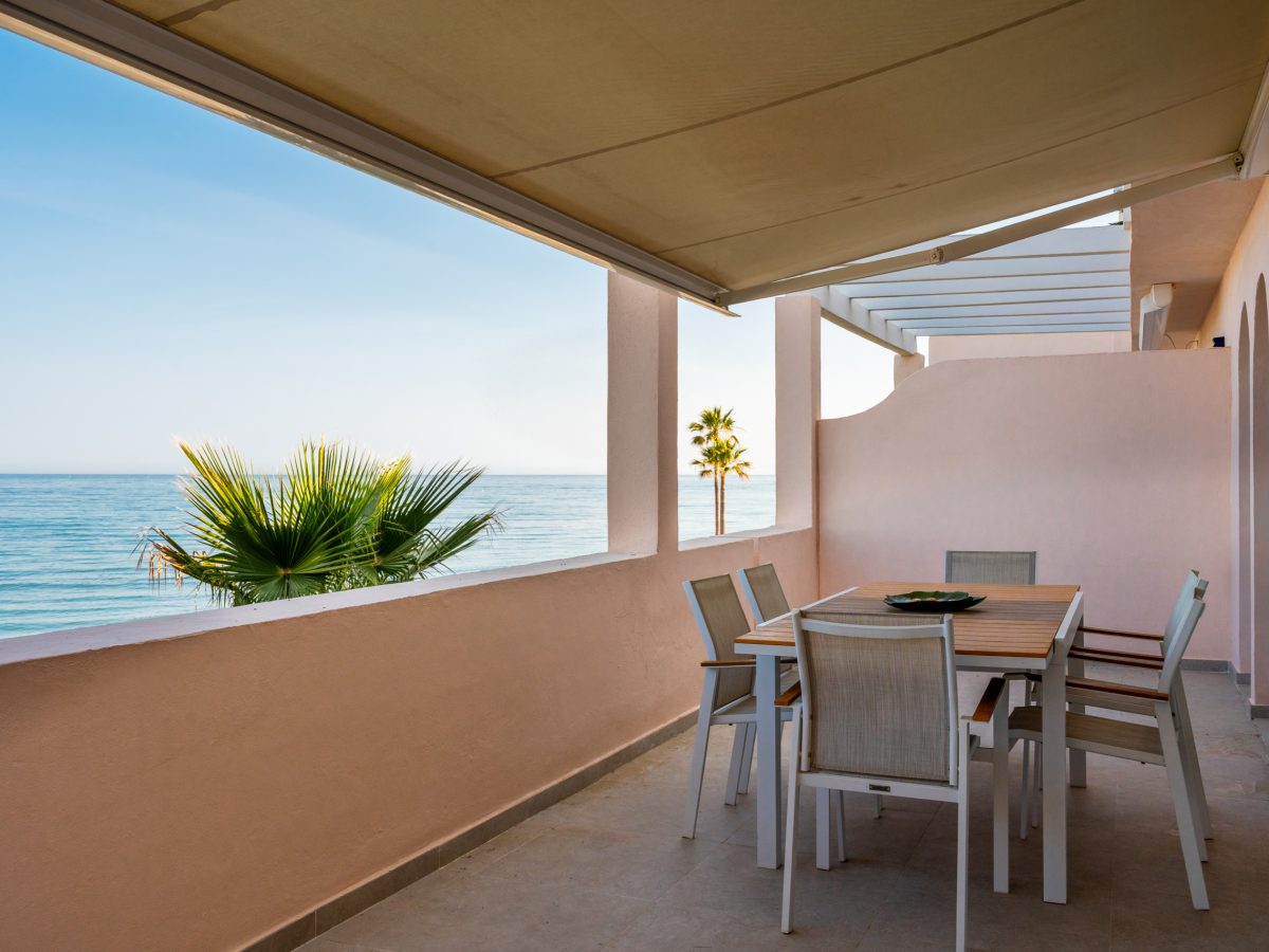 Seafront terrace with outdoor dining area, awning, and Mediterranean views at Playa del Moral apartment.