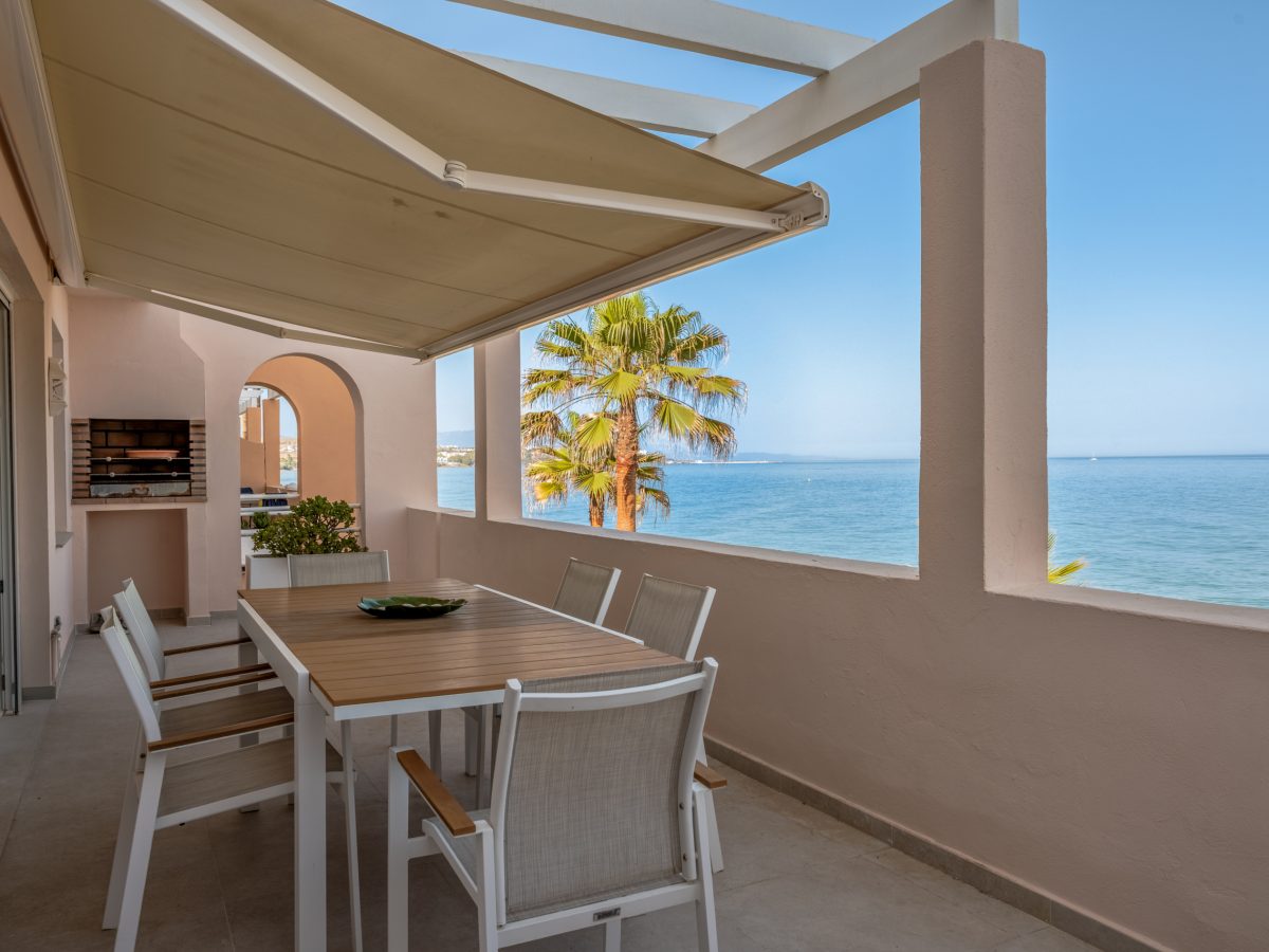 Seafront terrace with outdoor dining area, awning, and Mediterranean views at Playa del Moral apartment.