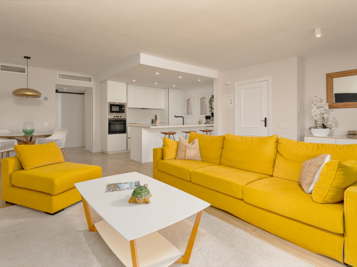 Bright open-plan living room with yellow sofa, modern kitchen, and dining area in Playa del Moral apartment
