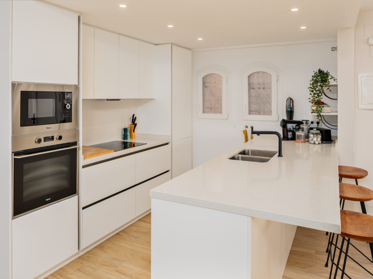 Contemporary white kitchen with breakfast bar, built-in appliances, and natural light in Playa del Moral apartment.