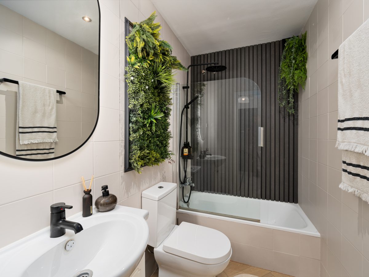 Modern bathroom in Bel-Air semi-detached house near Marbella with sleek black shower fittings, vertical wood panels, and green wall feature.