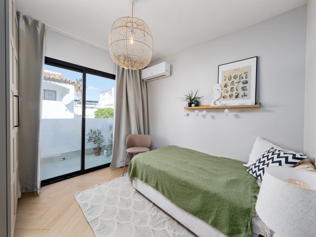 Bright guest bedroom in Bel-Air semi-detached house near Marbella, featuring minimalist decor, sliding glass doors, and neutral tones with green accents.