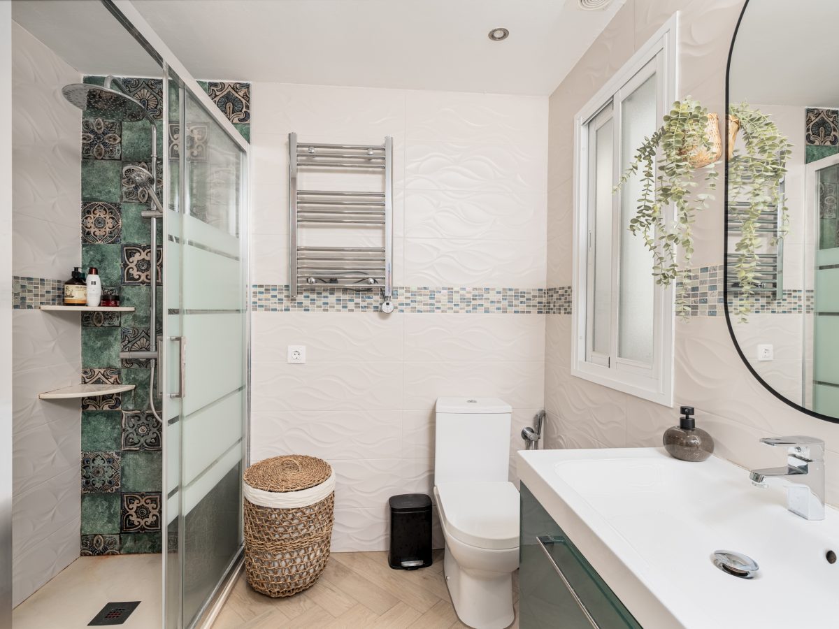 Modern bathroom interior in Bel-Air semi-detached house near Marbella, featuring glass shower, white tiles, green vanity, and decorative mosaic details.