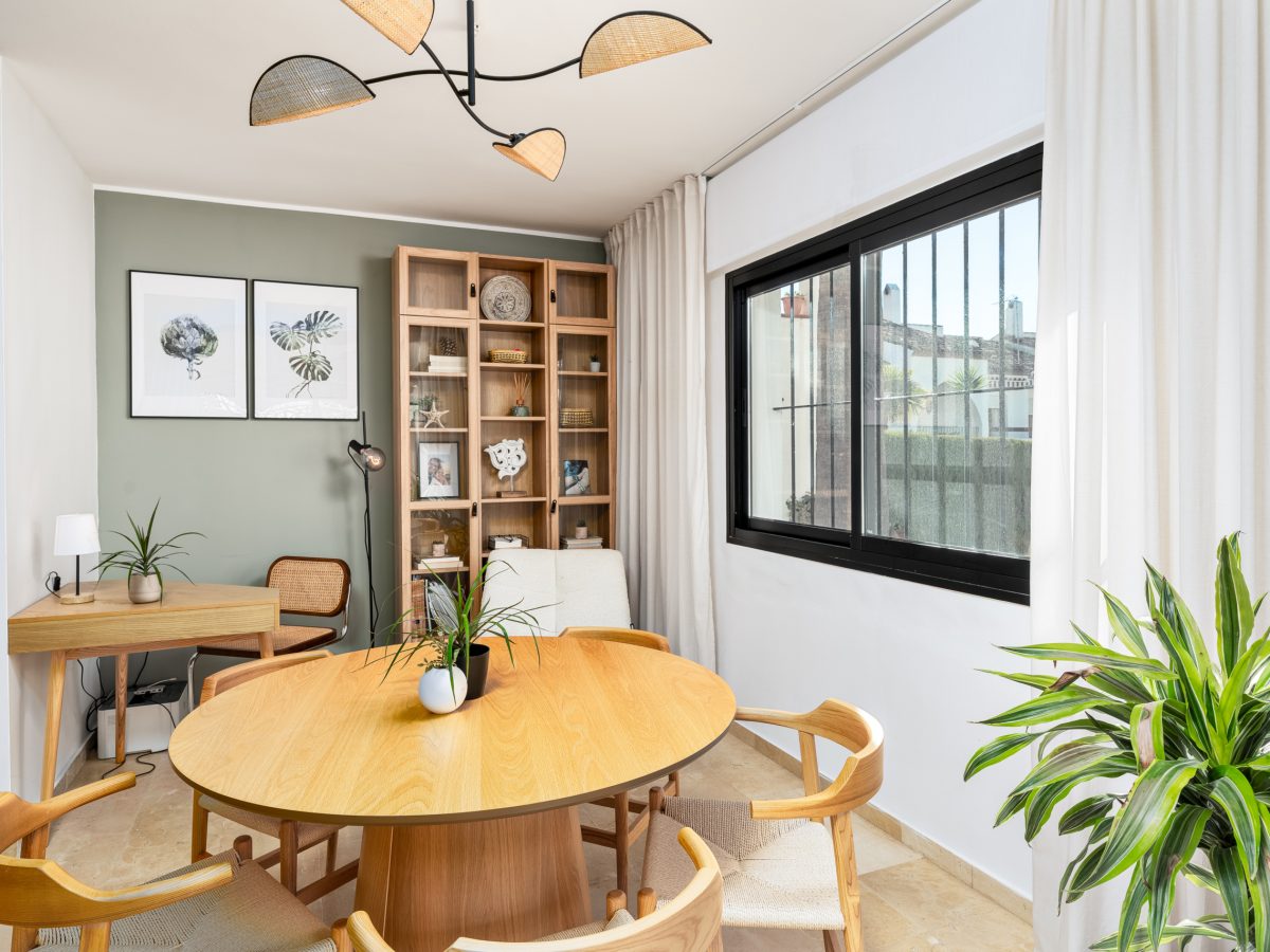 Bright modern dining room with wooden round table, mid-century chairs, indoor plants, and large window in Bel-Air semi-detached house.
