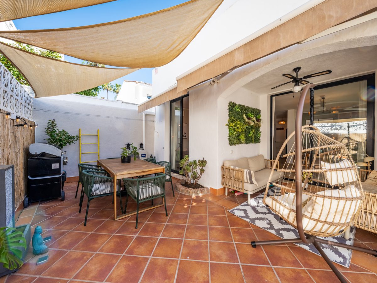 Stylish covered terrace at Bel-Air semi-detached home near Marbella, featuring terracotta tiles, outdoor dining area, hanging chair, and Mediterranean decor.