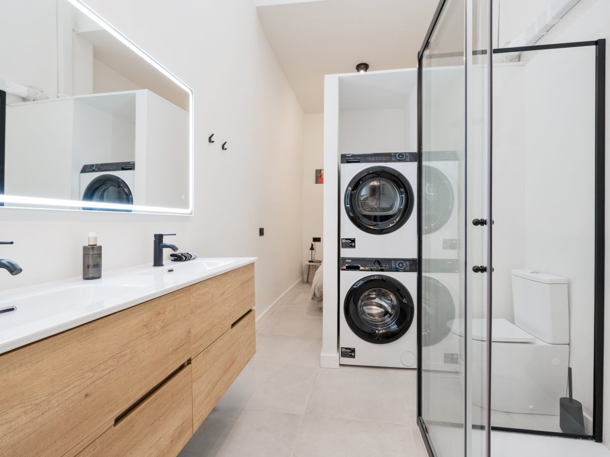 Modern bathroom with wood vanity, glass shower, and laundry area in Estepona old town apartment