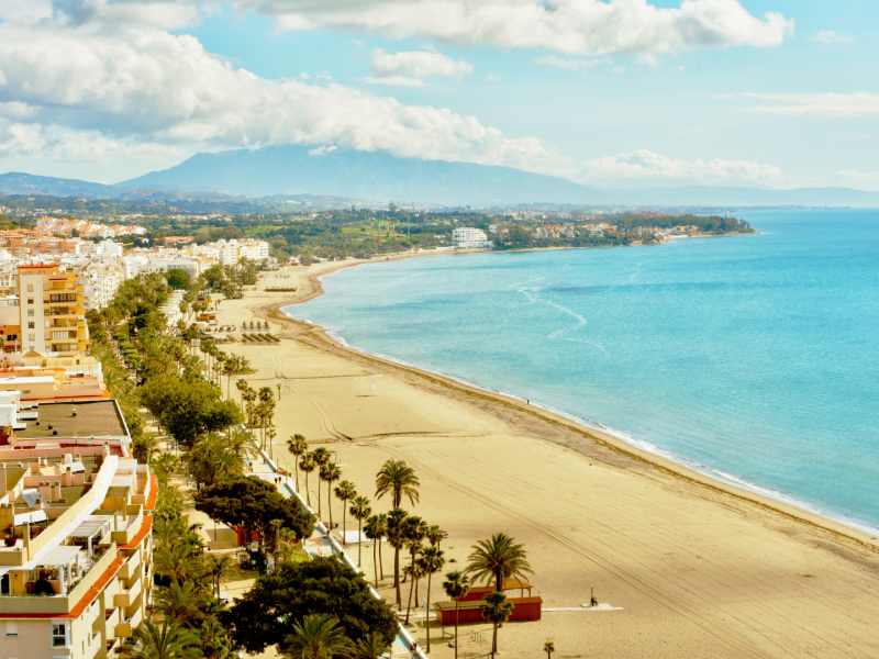 Aerial view of Estepona beachfront, Costa del Sol — golden sand, Mediterranean Sea, and palm-lined promenade near luxury apartments and villas-Quintessentia Propety Advisors