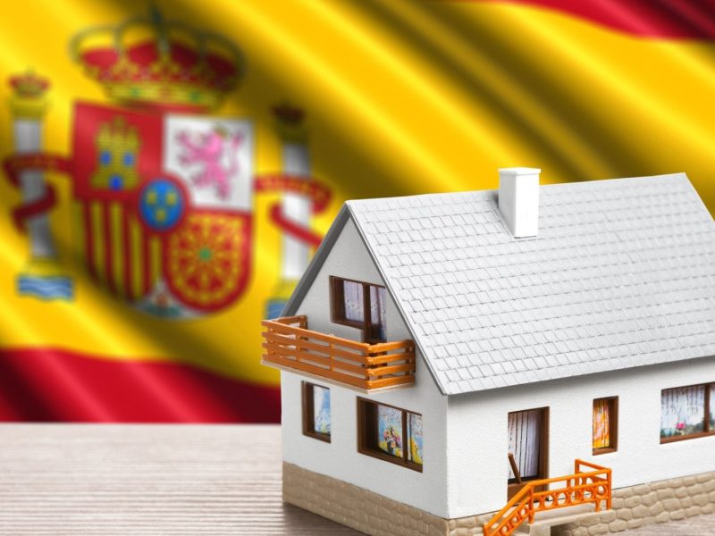 Model house in front of Spanish flag representing property ownership for non-residents in Spain.