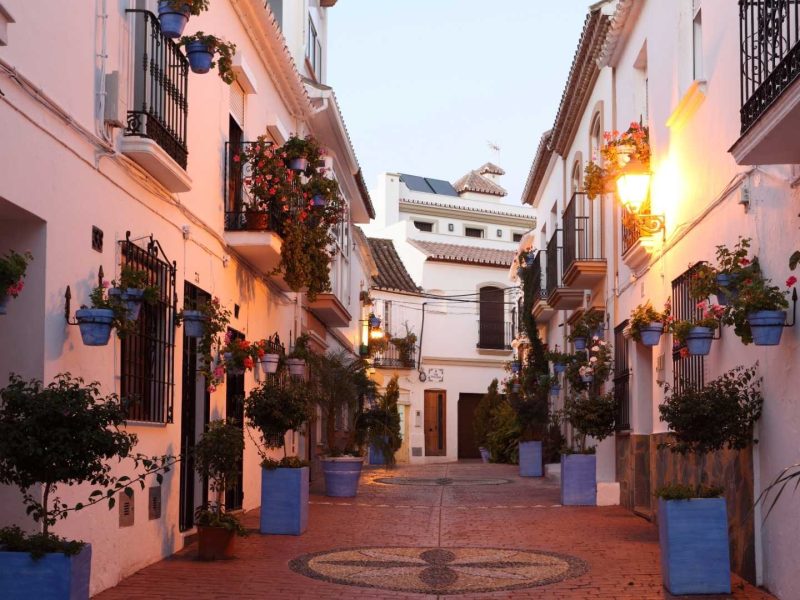 Charming traditional street in Estepona Old Town with whitewashed houses and flower pots, highlighting the area’s appeal for property investors in southern Spain and illustrating the average rental yields for properties in Estepona.