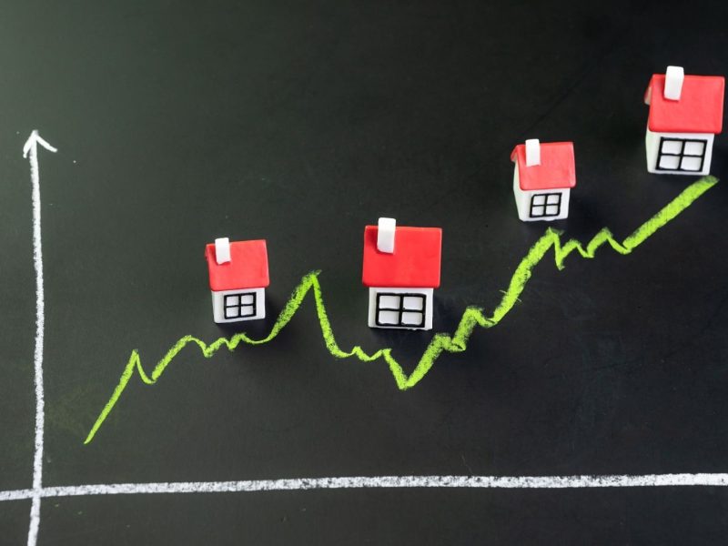 Rising property prices in Nueva Andalucía shown with miniature houses on an upward graph representing real estate market growth