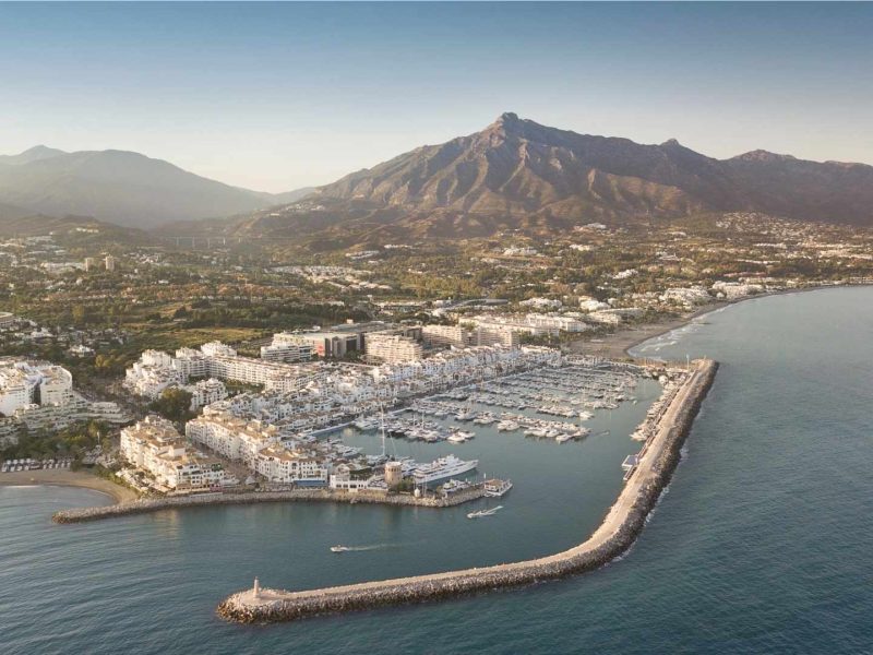 Aerial view of Puerto Banús marina and luxury neighborhoods in Nueva Andalucía, Marbella, with La Concha mountain in the background.