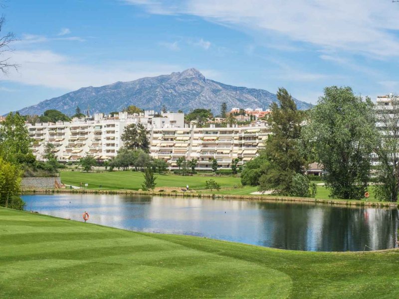 Golf course in Nueva Andalucía, Marbella, with mountain views and residential buildings overlooking a lake on the Costa del Sol.